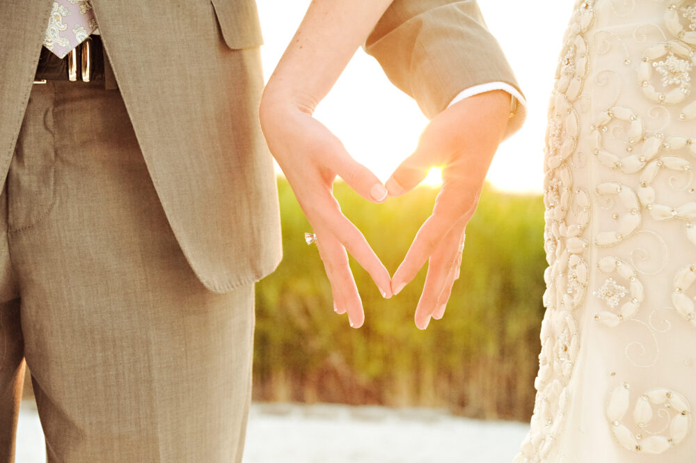 A bride and groom making a heart shape with their hands.