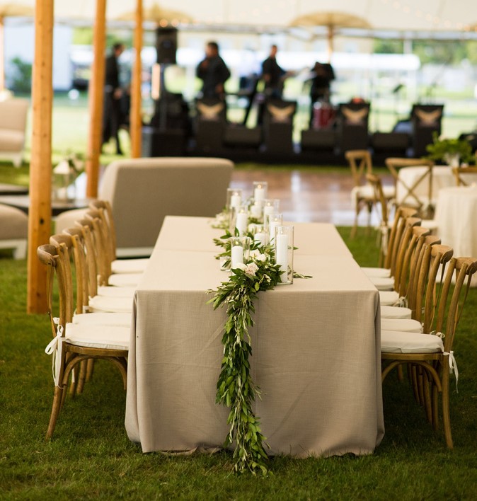 A table set up in a tent with white linens and greenery.