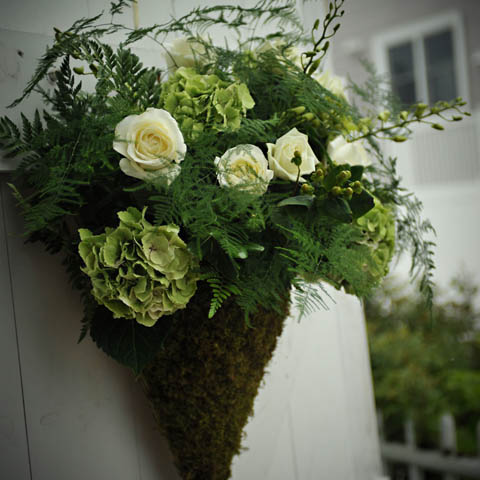 A green and white flower arrangement hanging on a wall.